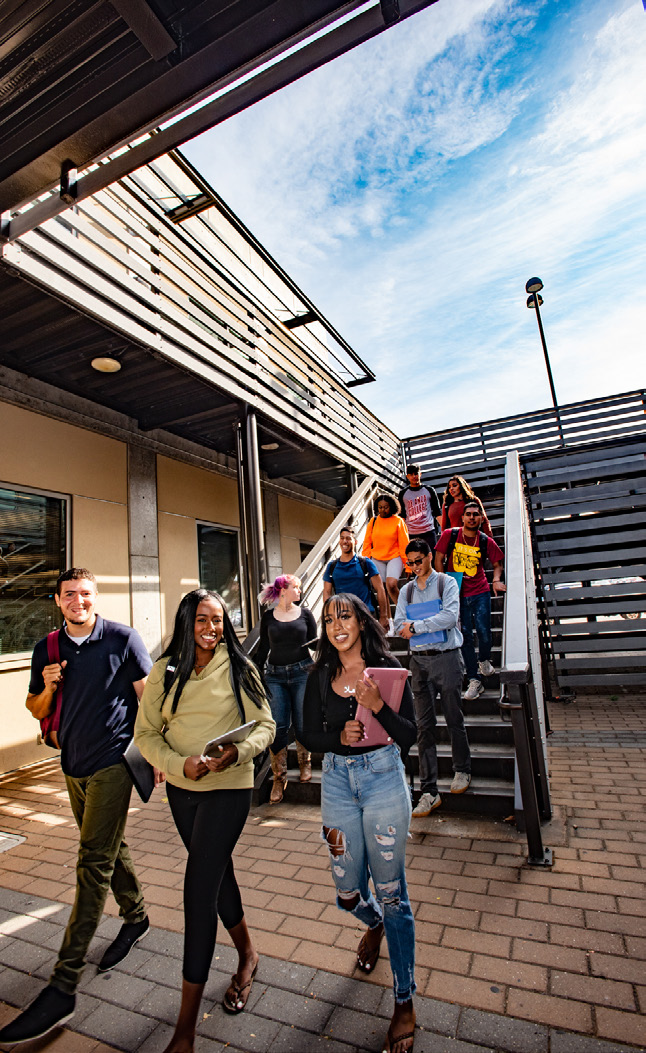 Students walking down an outdoor campus staircase, carrying books and tablets.