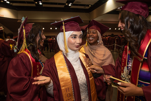 young women in grad caps laughing, one is wearing a white scarf