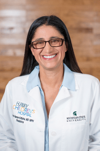 Dr. Mona Hanna in her medical coat wearing classes smiling.